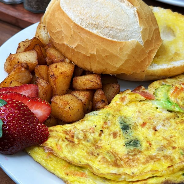 Brazilian breakfast with omelet, home fries, strawberries, and a buttered roll on a white plate.
