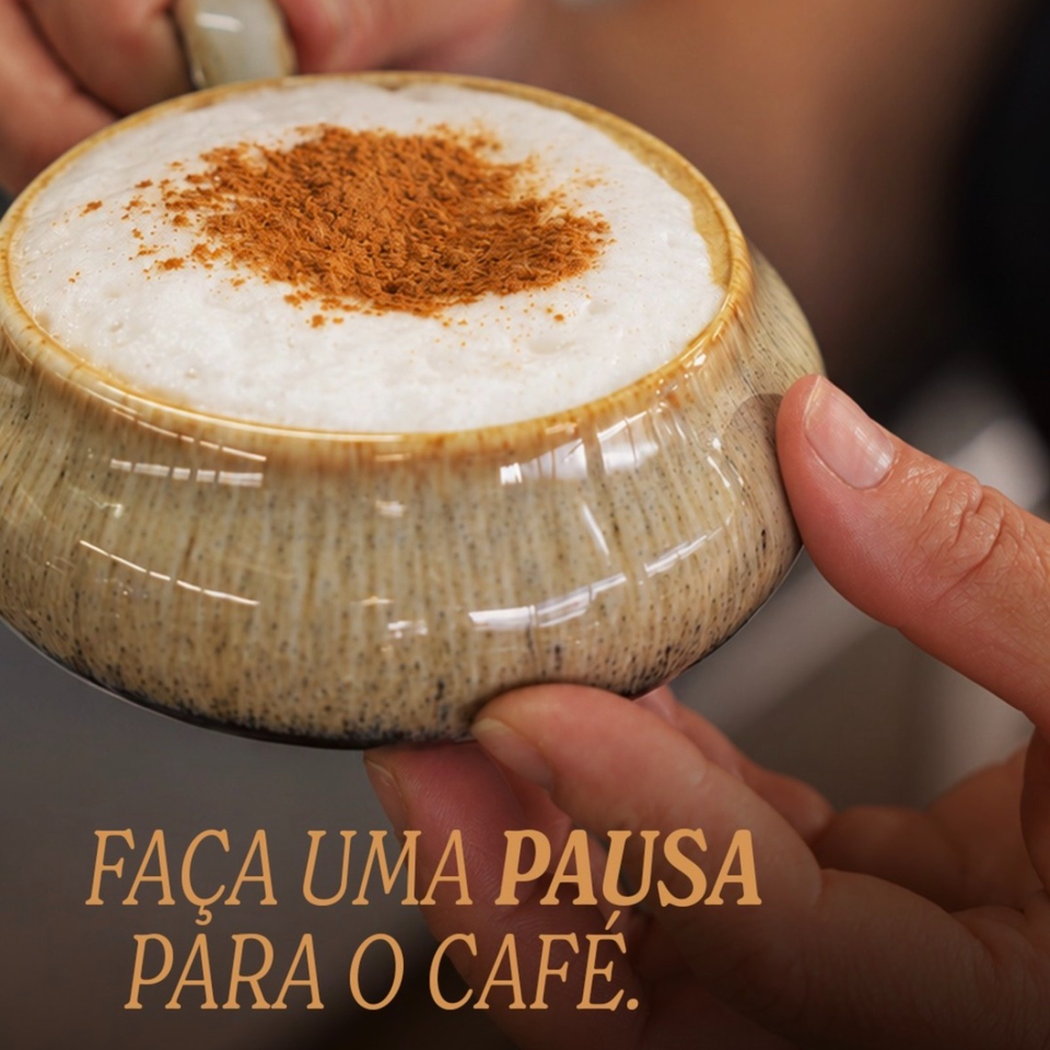 Hands hold a speckled ceramic cup filled with frothy coffee dusted with cinnamon.