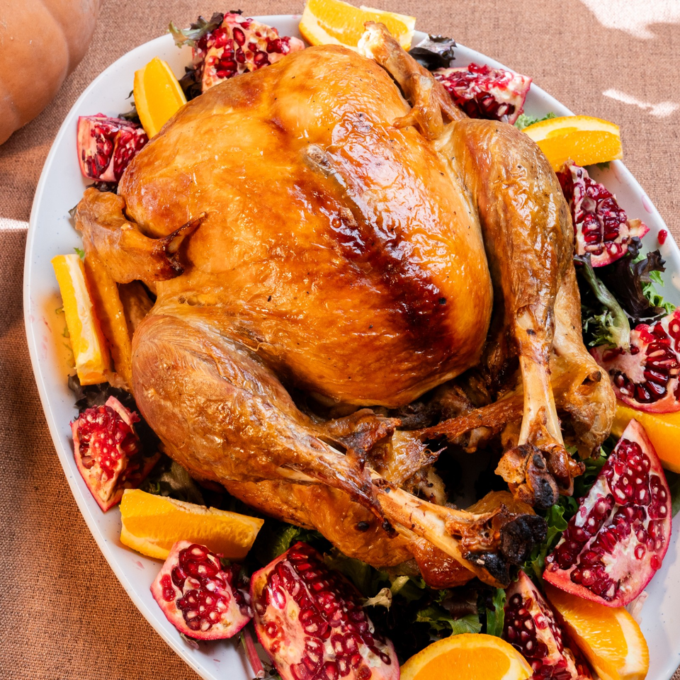 Golden roasted turkey surrounded by orange wedges, pomegranate halves, and leafy greens on a large platter.