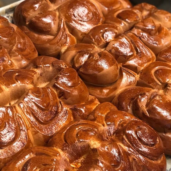 Close-up of a tray of freshly baked, glossy, golden-brown Brazilian sweet bread rolls.