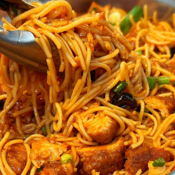 Tongs lifting Brazilian-style spaghetti with chicken, olives, and green onions in a rich sauce.