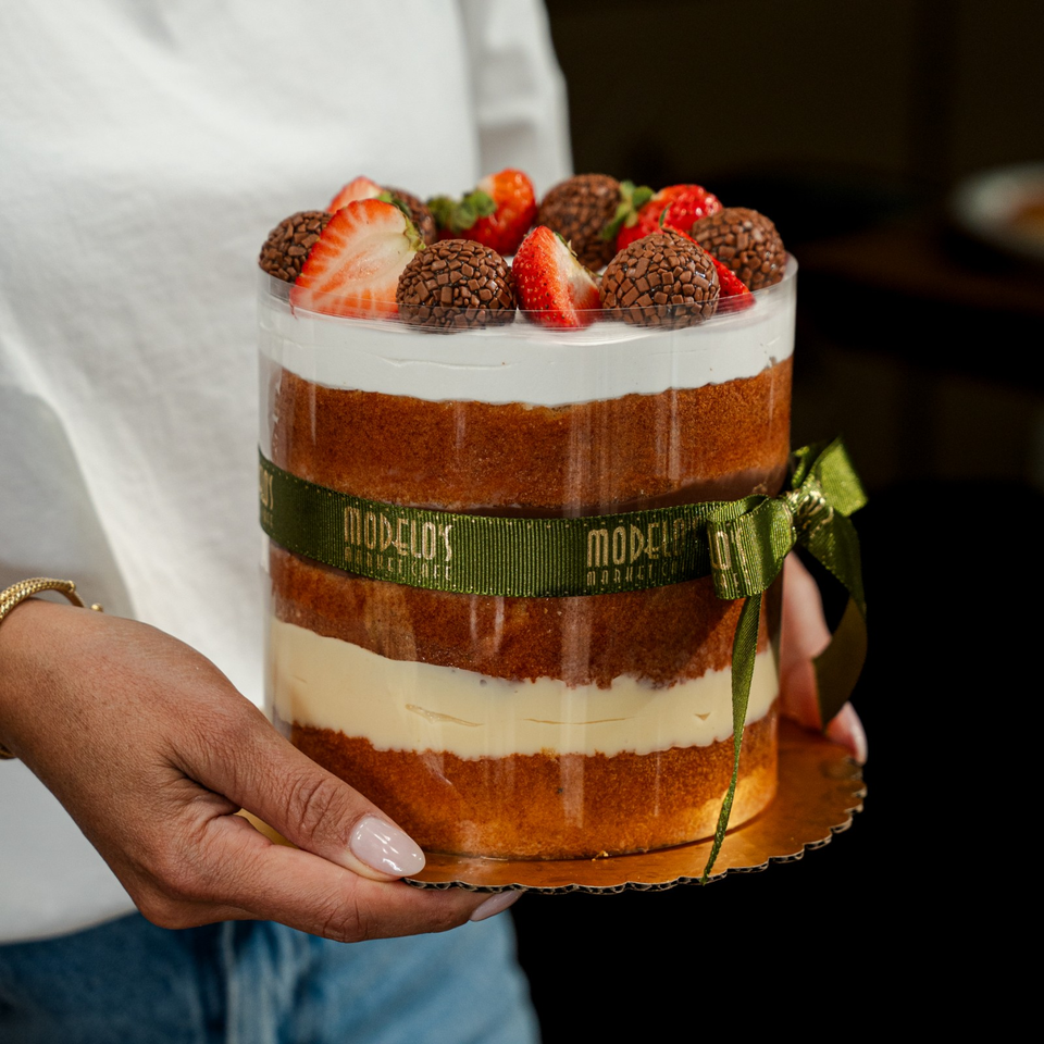 Layered cake with white cream, chocolate-covered truffles, and strawberries, presented on a platter with a green ribbon.