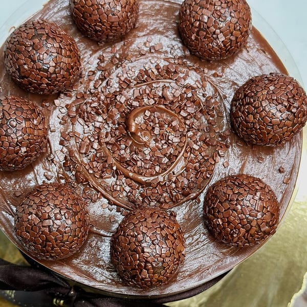 Overhead view of a chocolate cake topped with Brigadeiro balls and chocolate sprinkles.