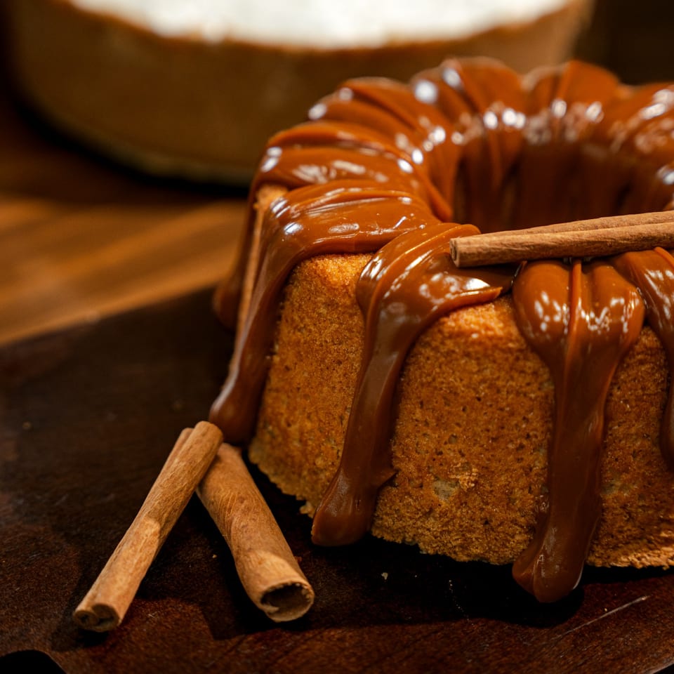 Bundt cake drizzled with caramel sauce and garnished with cinnamon sticks on a dark wooden table.