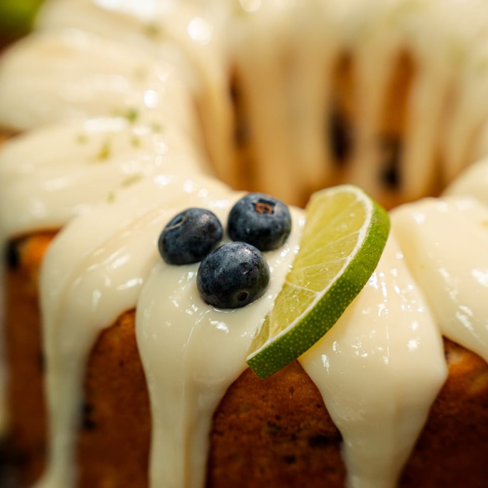 Close-up of creamy dessert topped with blueberries and a lime slice on a wooden table.