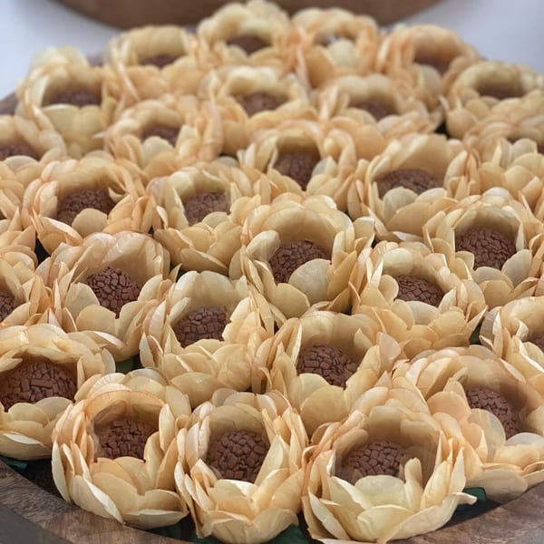 A close-up of many Brazilian Brigadeiro chocolate truffles in light yellow paper cups.