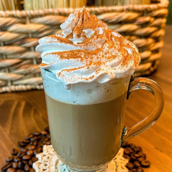 Modelo's Market Cafe's coffee drink with whipped cream and cinnamon, surrounded by coffee beans.