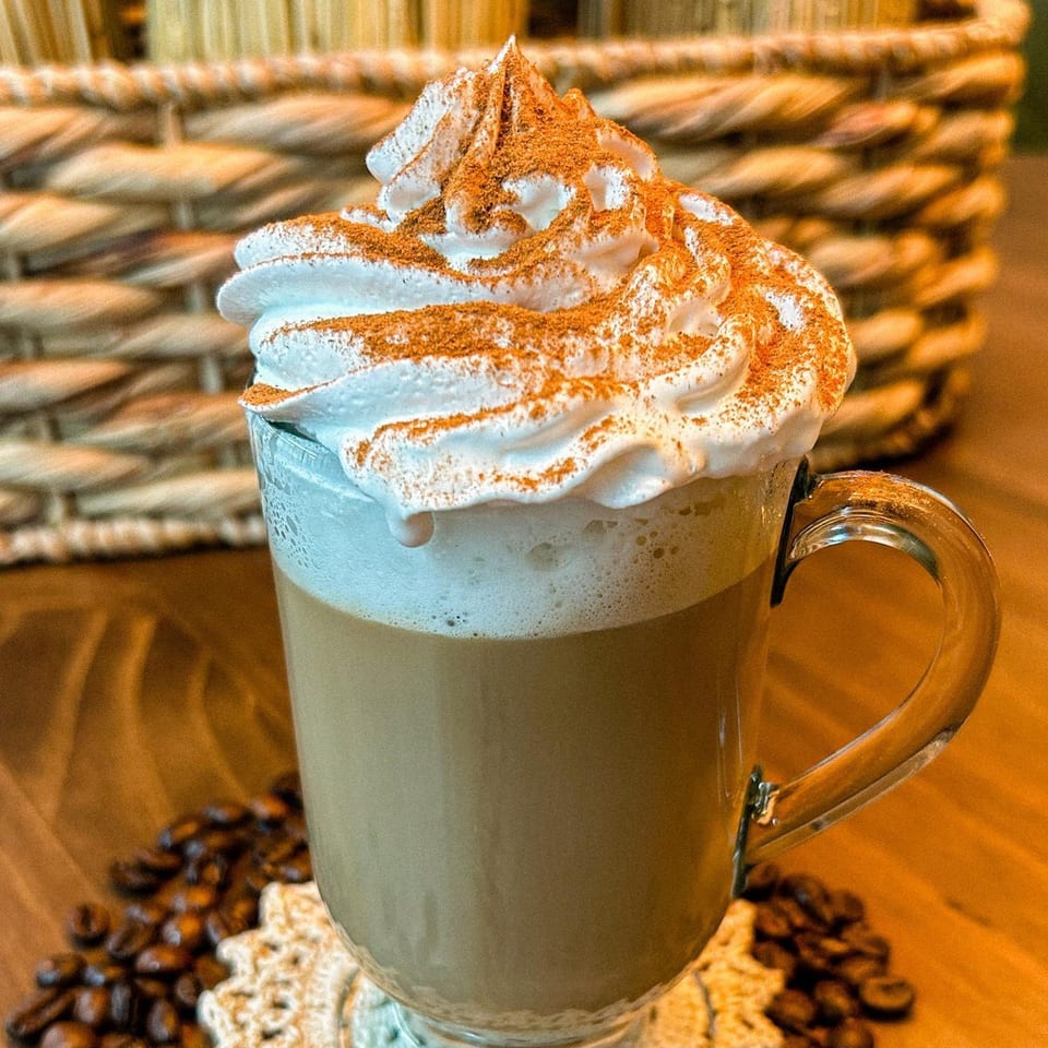 Modelo's Market Cafe's coffee drink with whipped cream and cinnamon, surrounded by coffee beans.