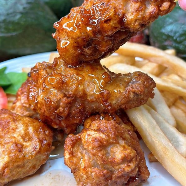 Crispy, glazed chicken wings with honey dripping, served with golden french fries on a white plate.