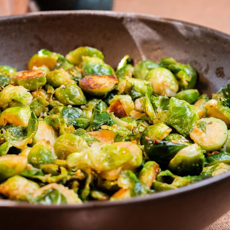 Roasted Brussels sprouts, halved and caramelized, fill a rustic brown serving bowl.