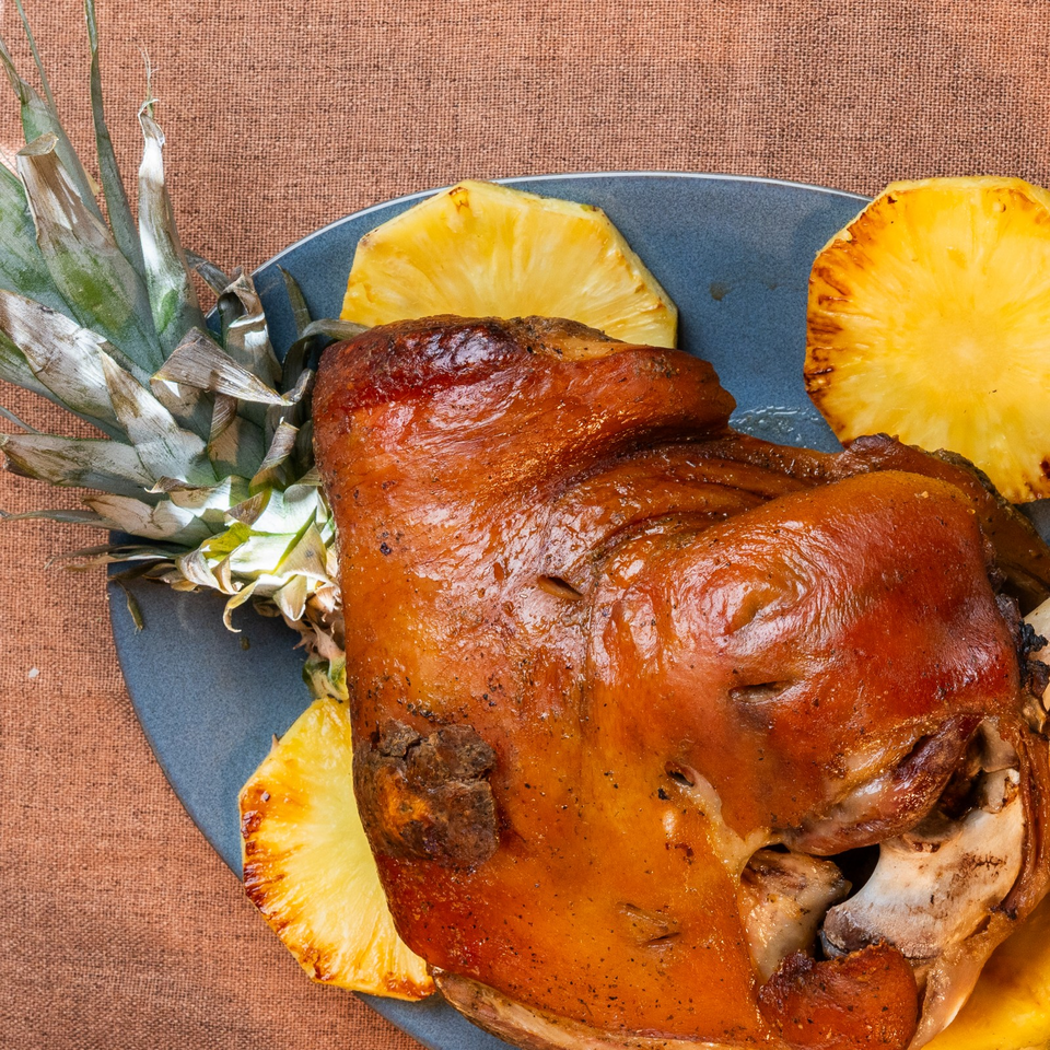 Roasted pork served on a blue plate with grilled pineapple slices and a pineapple crown.