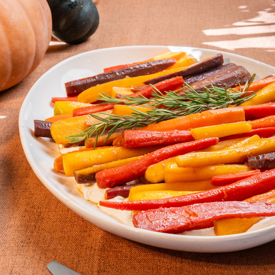 Roasted rainbow carrots arranged on a platter with fresh rosemary, beside pumpkins on a rustic table.