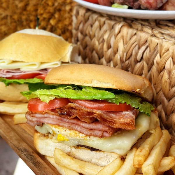 Two Brazilian sandwiches with ham, cheese, lettuce, tomato, and bacon, served with fries.